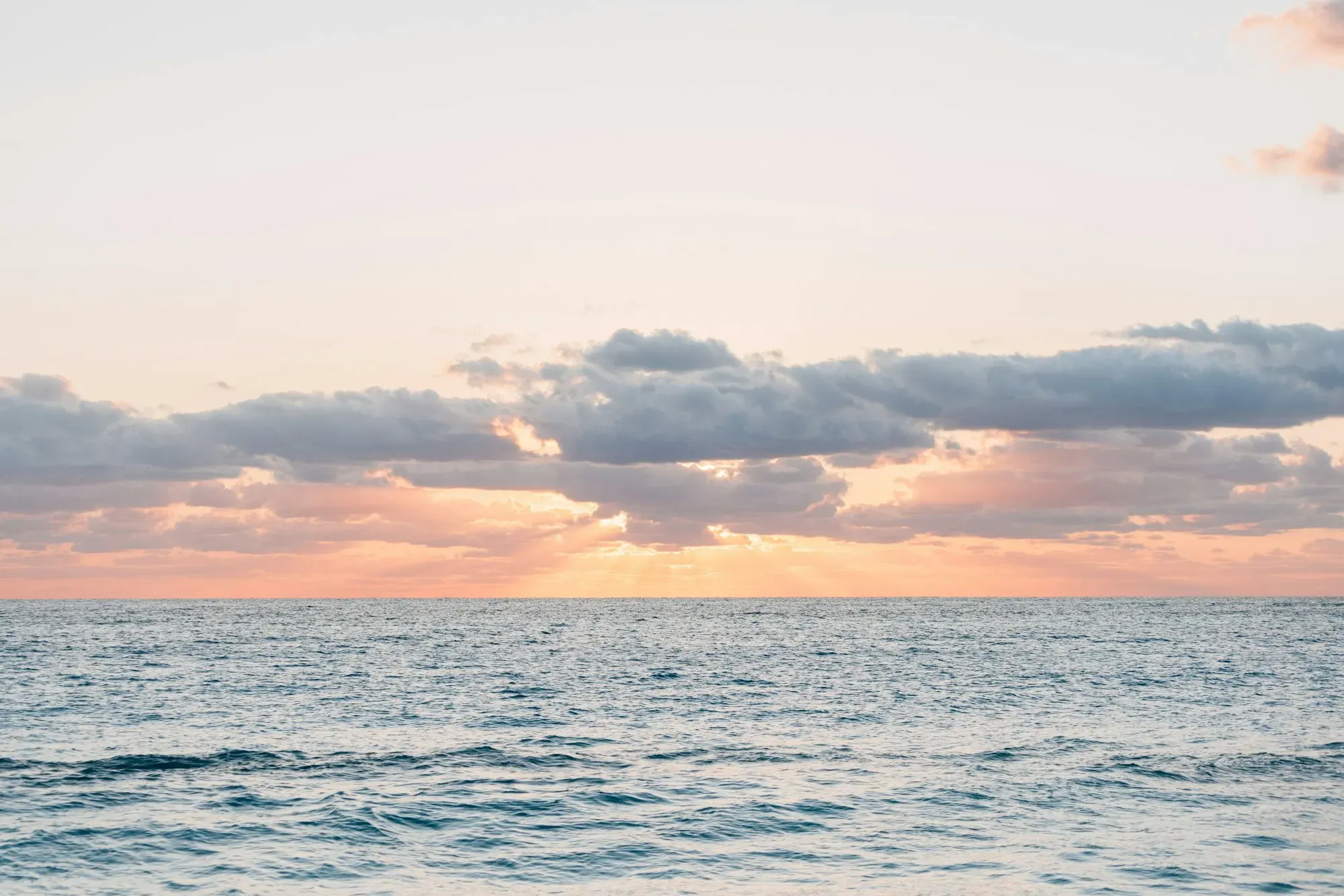 A calm sea at sunrise under a warm, soft sky