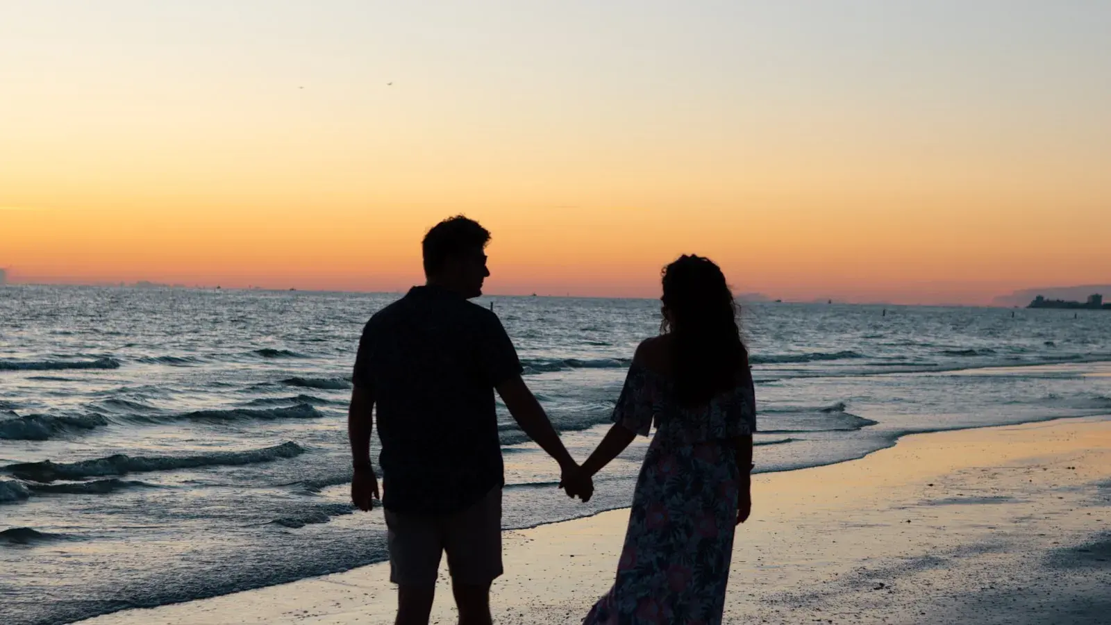 A couple holding hands as they walk together along the beach at sunset
