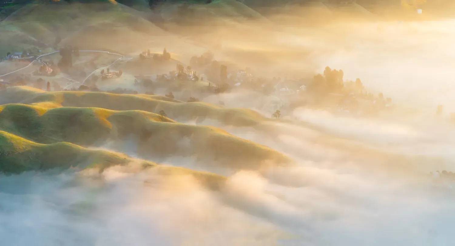 Soft golden light over misty rolling hills at sunrise
